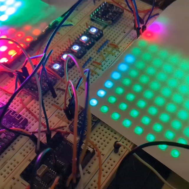 an electronics breadboard with some matrix panels. one has some rainbow swirlies, and another is green with a green-blue bar showing the volume.