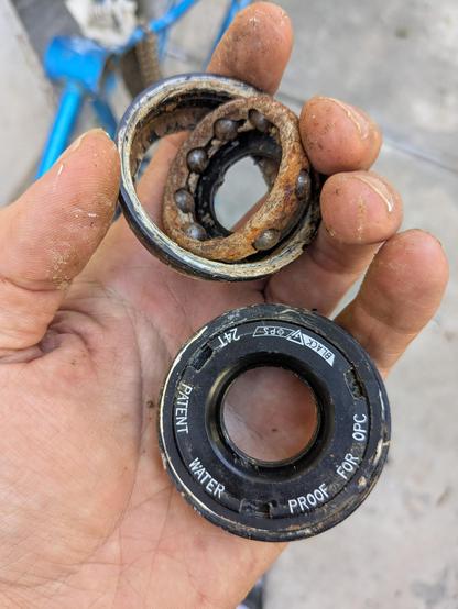 a bottom bracket bearing and inner race. the cage holding the bearings is heavily rusted. held near the outer bearing race labeled "patent water proof for opc"