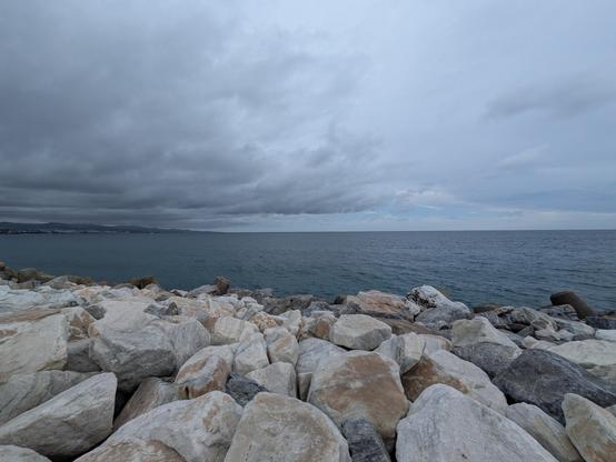 Looking out across large rocks on a calm sea under a cloudy sky