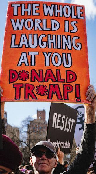 An anti-Trump protestor in Washington Square Park in New York City holds a sign that says, "The Whole World is Laughing at You, Donald Trump," while other signs say, "Resist," and #goodtrouble