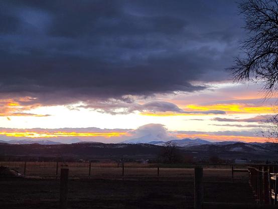 Dark sky at sunset with streaks of yellow & orange clouds above a mountain range.
