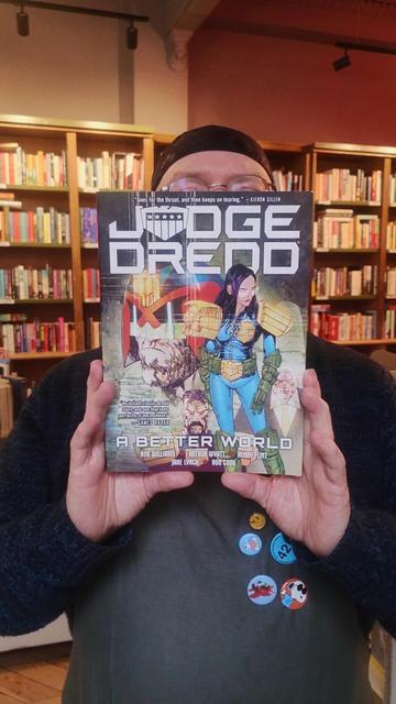 bookseller Joe holding up a copy of the Judge Dredd graphic novel, A Better World, to recommend it in the Edinburgh Bookshop