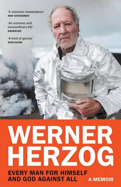 Cover of Werner Herzog's memoir "Every Man for Himself and God Against All". It shows a photo of Herzog on the set of "Into the Inferno", his 2016 documentary about volcanoes. He's wearing a shiny silver lava suit and is holding its cylindrical helmet in front of his chest. He's looking into the camera with an intent but neutral expression. Volcano smoke billows behind him. Below this image, his name and the book title are in uppercase sans-serif text in white and black on a red background.