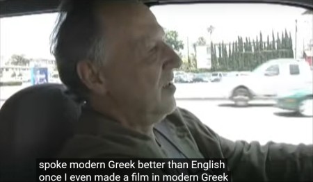 Image of Werner Herzog driving a car, saying to his unseen passenger, 'I spoke Modern Greek better than English once. I even made a film in Modern Greek.'
