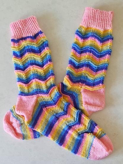 Pair of hand-knitted socks. Heel, toes, & cuff are pink. Main body of sock is striped - purple, blue, lime green, yellow, pink.
Pattern is chevrons.
