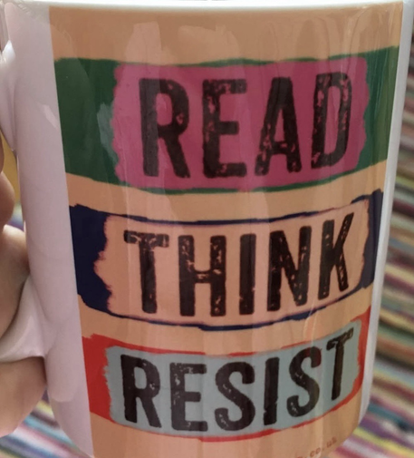 White mug with “Read Think Resist” printed on side. Words printed stacked on each other. Read on pink strip on green, Think on beige strip on navy, and Resist on grey strip on read. All 3 words on strips arranged on beige rectangle printed in mug’s side. From Four Leaves Bookshop in Nottingham, UK.