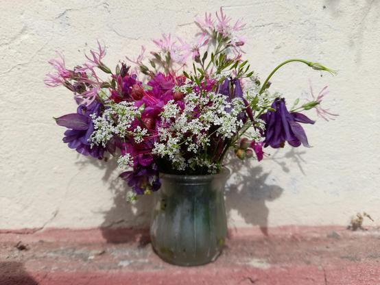A small glass vase with a bouquet mixed with wild and garden flowers, in white, pink and purple.