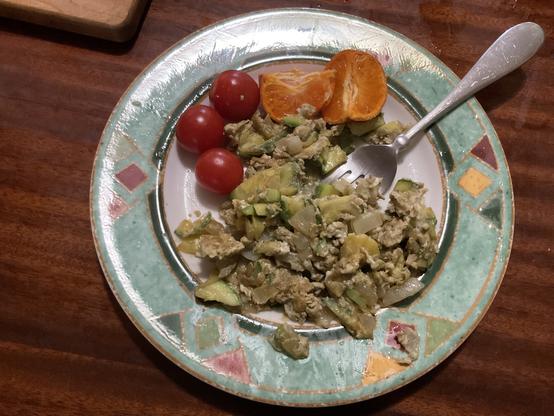 Scrambled eggs, zucchini, onion. couple of cherry tomatoes and bit of orange on a plate.