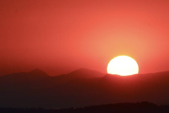 The sun dipping behind hills on the horizon with a bright orange glow
