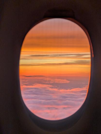 Vivid sunset colours with layers of clouds above and below, viewed through an airplane window.