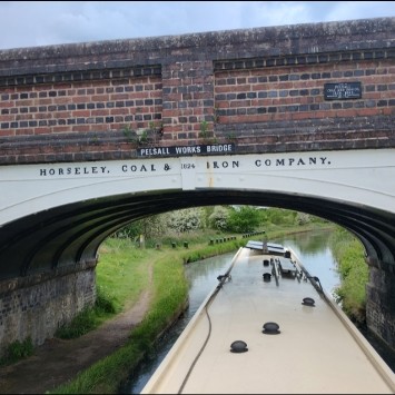 A steel-arched canal bridge that is level on top, and has a brick parapet (the sides, like railings, but formed of a brick wall). The brick has some decorative detail, where bricklayers showed their skill.

In the photo, a narrowboat is passing under the bridge, and the photo was taken looking forward ober its roof.

The bridge's signage, facing all boats passing below, dates back to Britain's industrial revolution. The largest sign reads: "Horseley Coal & Iron Company 1824" as black letters spaced across several meters of the white arch. A second sign reads: "Persall Works Bridge" and this sign resembles the signage on all bridges in this area, which are named, not numbered. There's a third sign that reads: "Site of Pelsall Iron Co. 1832 - 1892. Presented for the millennium, 994 - 1994". (Those last digits are very small and I may have misread them.)