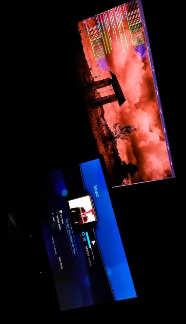 The photograph composed in total darkness, features two large screens against a black background. The top screen displays a vivid image of a Sepia sky with clouds and a structure resembling a Sluis, gazebo or pavilion, with colorful text overlays at the top. The bottom screen shows a blue interface with the word "Music" in white text, indicating a music player. It displays the song "I've Got You Under My Skin" by Michael Bublé, with a playback time of 00:08:01 out of 01:09. A smaller screen within the bottom interface shows a person, likely the artist, with the album cover visible. The overall setting suggests a music streaming or playback environment.

 Ovis2-8B

🌱 Energy used: 0.177 Wh