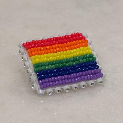 A beaded rainbow pride flag pin edged in rhinestones on a white background