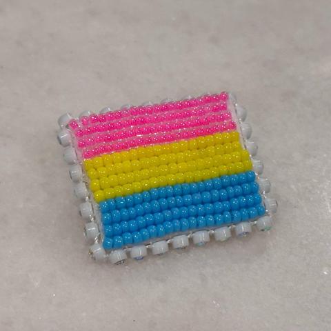 A beaded pansesxual pride flag pin on a white background