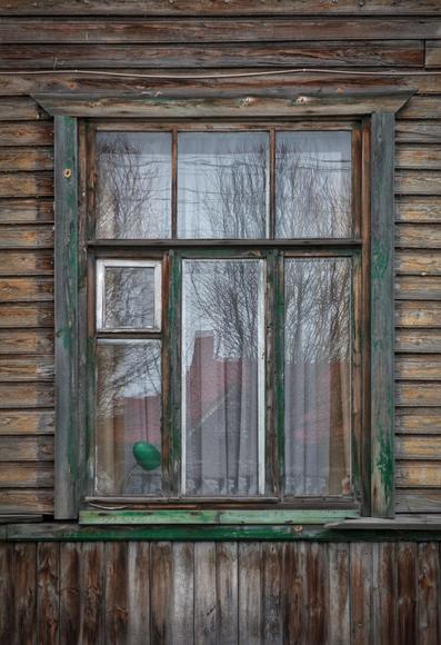 An old window of a wooden shabby house. There is a green old lamp on the window.