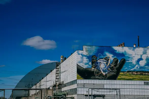 A mural on the side of Chernobyl's power plant, next to the sarcophag, depicting a gloved hand releasing an atom in a blue sky landscape.