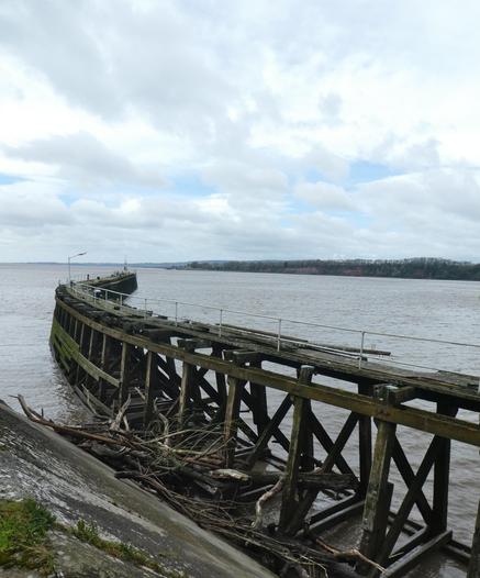 A rickety, curved pier jutting out into a river estuary.