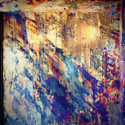 Blue, purple, and gold paint chip away to reveal bright, metallic layers of each other underneath, framed with large bolts screwed into the surface's corners.