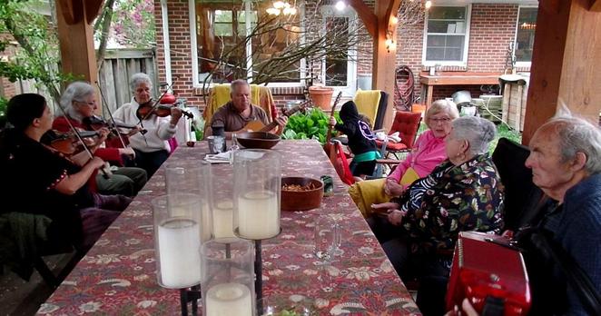 Three fiddlers, a guitar player, a spoon player, an accordionist and some onlookers attend an outdoor fiddle jam on World Fiddle Day in Ontario.
