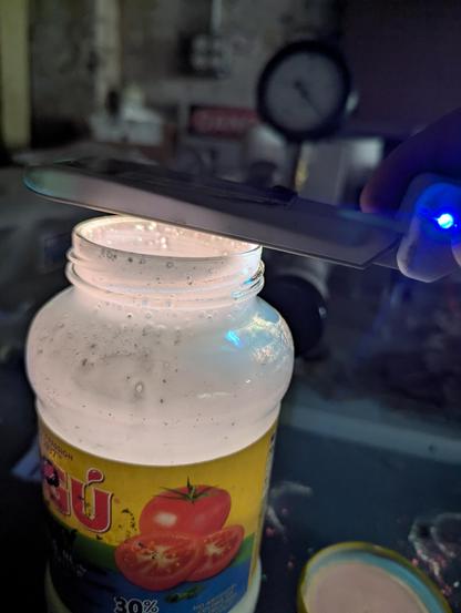 An old RAGU jar coated with a speckly coating of warm white light. Bkue light from the Argon mercury quartz tube above. Manifold in the background.