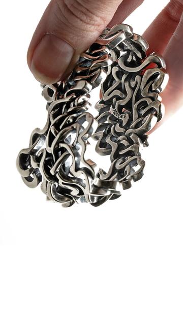 A hand holds a solid sterling silver napkin ring by Xover0. The design interweaves seven historic courses of the Mississippi River into a rhythmic and dynamic sculpture.