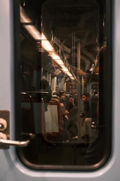 Picture of a group of people chatting on the subway, during a ride. On the right is also visible a hand, holding onto a pole. The picture is taken through the doors between two train cars.
