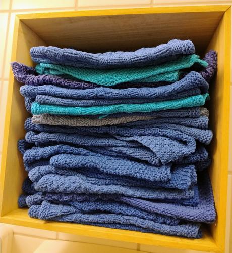 A small wooden shelf filled with folded hand knit towels, mostly royal blue but some in turquoise and other shades of blue.