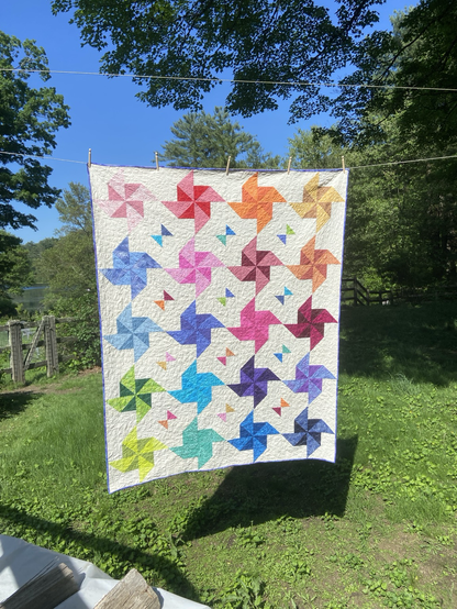 Quilt hanging on a clothesline with multi color pinwheels on a white background.