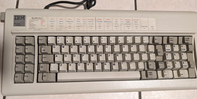 Image of an IBM 5160 Model F keyboard, It's a bit dirty but in overall really good shape. It has a Wordperfect cheat sheet glued aove the number keys.