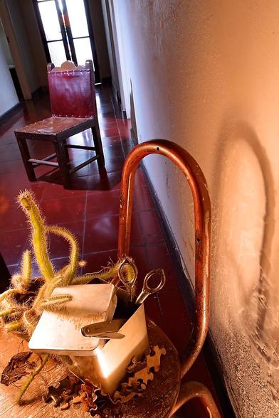 Color photograph of entrance hallway. Red floor and salmon walls lead to a backlit privacy glass door. Near the camera a broken plywood and metal tube small school chair holds a small cactus and partly open shiny aluminum square box. A tiny childs pocket knife and repaired mending scissors protrude from it. Closer to the door an even older heavy wood and leather child-sized chair stands on the glass door reflection. General feeling of magic and child-like wonder. EOS D60 (6.3 MP!) Sigma 14mm EX @F11/, 60 sec exposure. Series taken in 2003 at my grandmothers house after she passed away and her closets were opened, revealing a lifetime collection of objects and memories.