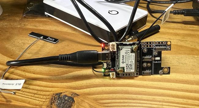 A mangling of wires and an electronics board. Two small lights are blinking green and red. A keyboard is in the background