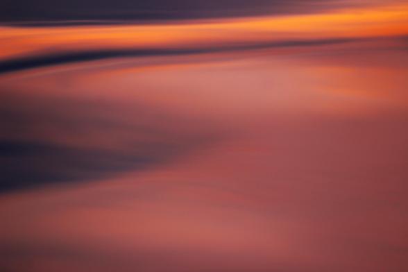 Sunset photo of a wide swath of reflected sunset light on the surface of a lake. The image has pink and violet light with an orange stripe across the top.