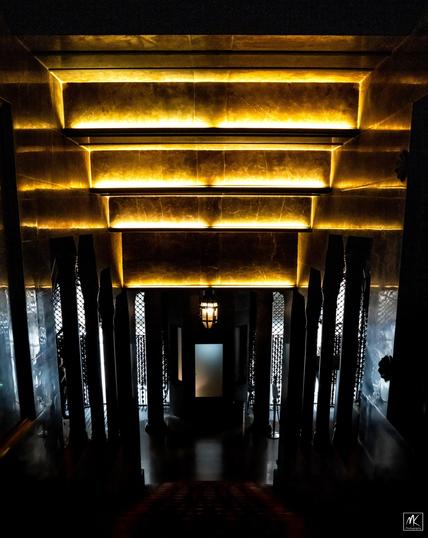 Inside looking down a dark staircase towards the entrance of #Gaudí’s Palau Güell with a golden geometric ceiling above.