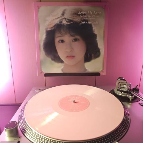 A pink vinyl record sits on a turntable. Behind the turntable, a vinyl album outer sleeve is displayed. The front cover shows a head shot of Seiko Matsuda looking at the camera.