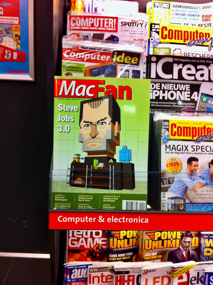 Photo of magazines in book store rack, including a 2010 Apple magazine cover, featuring a voxel-style Steve Jobs statue, being built by Pixar characters.