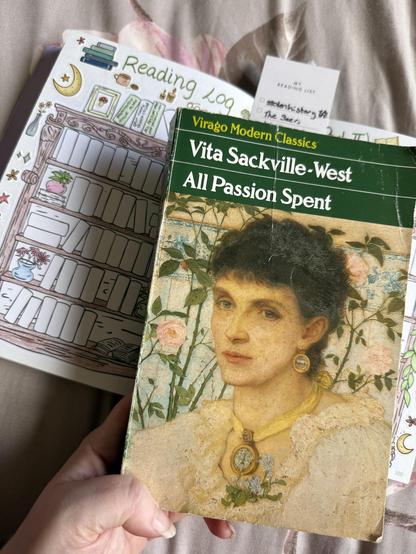 A hand is holding a copy of "All Passion Spent" by Vita Sackville-West, featuring a portrait on the cover. In the background, there is a reading log with decorative bookshelves and a bookmark with a checklist.