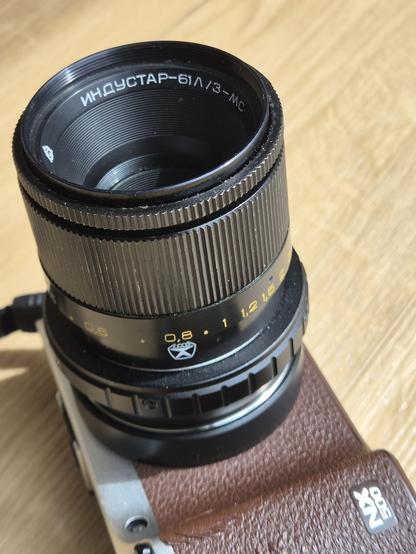 A diagonal photo of a black Industar lens, connected to a brown and aluminium camera lying on its back. The lens has a cyrillic imprint in the inner funnel and a characteristic "Made in the USSR" star logo. The camera is a Samsung NX500.