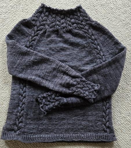 A gray sweater with knit cables on a high neck, two cables going down the side through plain stockinette knitting. The sleeves are stockinette until the cuffs, which are cabled again. The cables plus bind off make the sleeve edges ruffly.