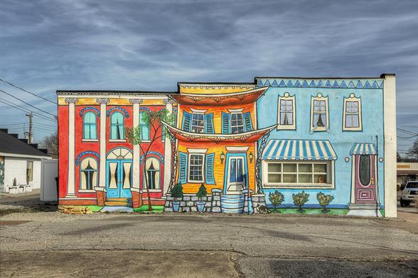 Vibrantly colored murals adorn the side of a building, depicting whimsical storefronts with lively facades.