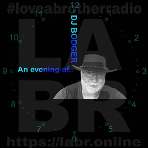 Black Background. LABR Logo in deep dark grey. #lloveabrotherradio on top. https://labr.online on the bottom.  A army green colored clock with numbers and dots covering the entire image. The hand set at 9 o'clock is the short hand and the hand is made out of the name of the show. "And hour of..." The min. hand set at the 12 and is made out of his name. DJ Bodger. A black & white picture of DJ Bodger. White British male with glasses, wearing an Aussie.  cowboy hat. Grey manicured beard. Black t-shirt