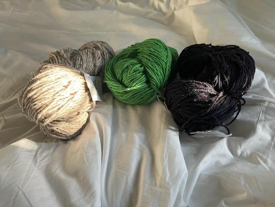 Three skeins of Irish tweed, the one on the left is oatmilk, the one in the middle is green and the one on the right is navy blue. All three have colour speckles, as tweed wool should.