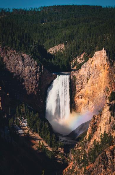 A waterfall in the middle of the scene with sloped terrain and trees around and a rainbow in the lower right corner.
