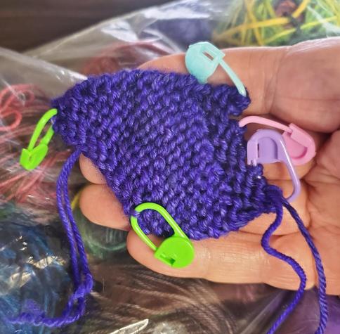 One half of a chickie wing in purple, with colorful stitch markers attached
