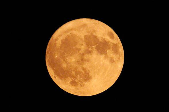 Photograph of a large full moon, tinged creamy yellow by wildfire smoke.