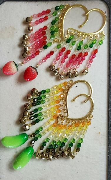 2 pairs of ear cuffs with beaded attachments hanging from them. the pair at the top has green, clear, red, and pink beads ended by small bells except for at the bottom where it's ended by a strawberry charm. the pair at the bottom has orange, yellow, clear, and green beads ended by small bells except for a the bottom where it's ended by a pickle charm