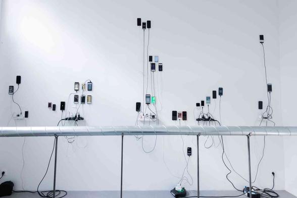 A lot of old phones stuck to a gallery wall. Various formations. Dangling cables.