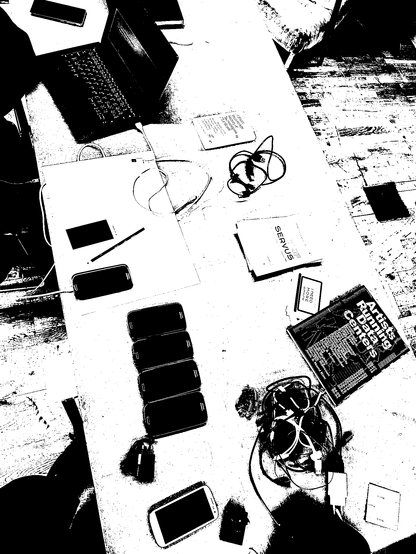 A table from above with a laptop, knots of cables, 7 smart phones and a book "Artists Running Data Centers".