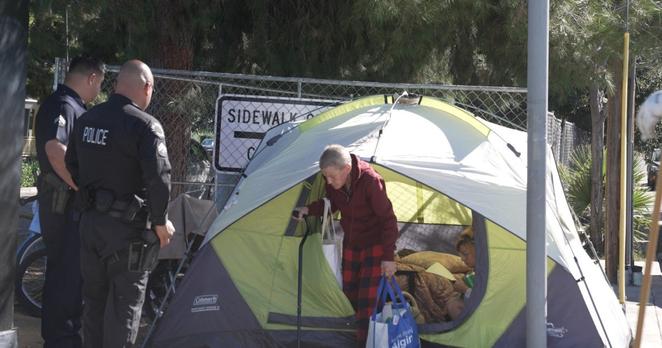 Police remove an unhoused woman from her tent