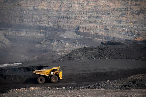 A yellow mining dump truck traverses a landscape blackened by coal.
