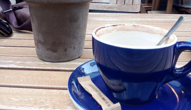 Une tasse de café bleue foncée, posée sur une coupelle de la même couleur et où se trouve un sachet de sucre. La tasse est vide, mais on peut y voir des traces de café. Elle, est posée sur une table en bois, juste à côté d'une plante dans un pot gris. Une tasse de café bleue foncée, posée sur une coupelle de la même couleur et où se trouve un sachet de sucre. La tasse est vide, mais on peut y voir des traces de café. Elle, est posée sur une table en bois, juste à côté d'une plante dans un pot gris.
